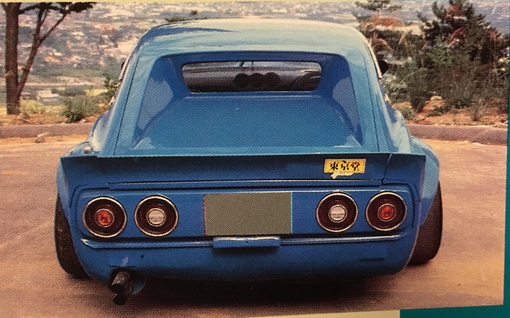 Rear view of a blue vintage car with round taillights and a Japanese sticker saying please keep your distance driving.