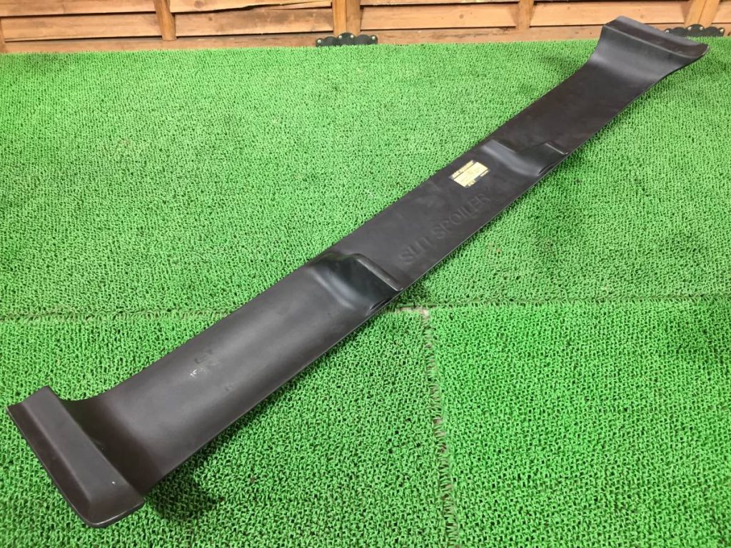 Black car rear spoiler on green artificial grass background, close-up view with 'SUN SPOILER' text embossed.