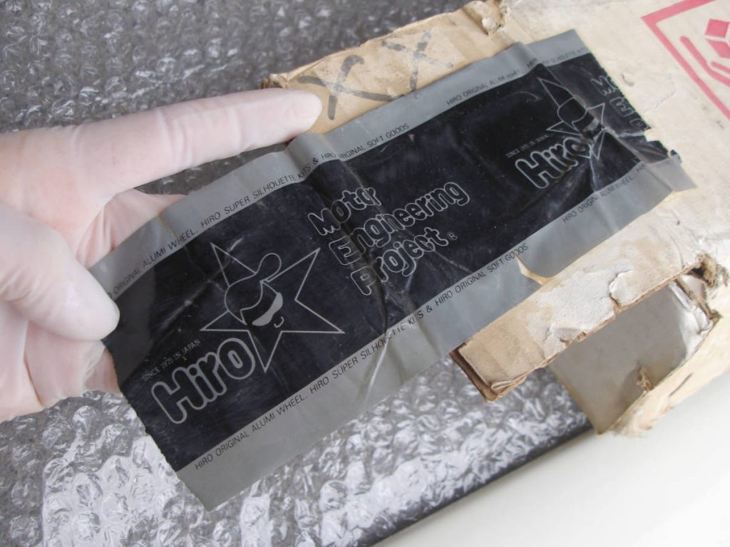 A gloved hand holding black tape with Hiro branding and Motty Engineering Project text against bubble wrap and cardboard.