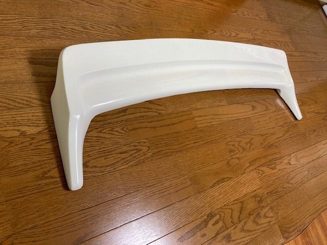 White car spoiler on wooden floor, potential aftermarket part for improved aerodynamics.