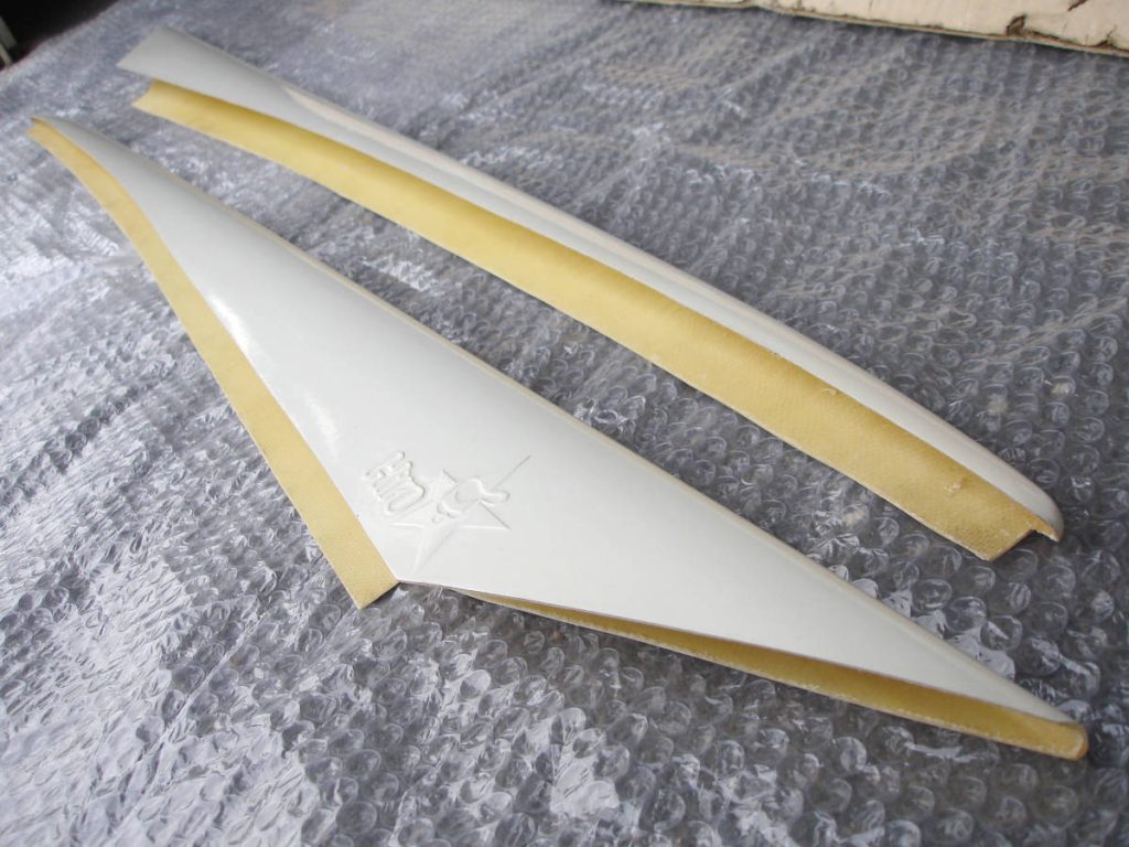 Close-up of two white and yellow fiberglas spoilers on bubble wrap with a Japanese HKS logo near the corner edge.