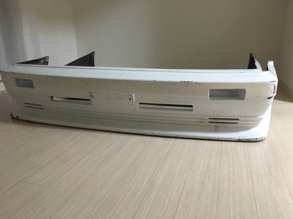 Used white front bumper for car, minor scratches, placed on wooden floor indoors.