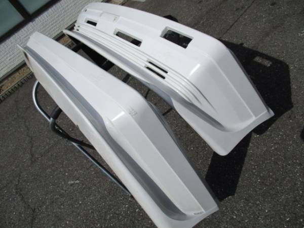White car bumpers displayed on the ground, showing front and rear parts, ideal for vehicle repair or replacement.
