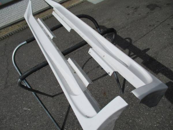 White side skirts for a car placed on a metal stand, viewed from the top at an angle, ready for installation.