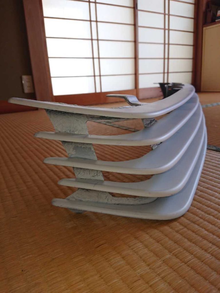 Car front bumper grill part on tatami mat in a traditional Japanese room with sliding shoji screen doors in the background.