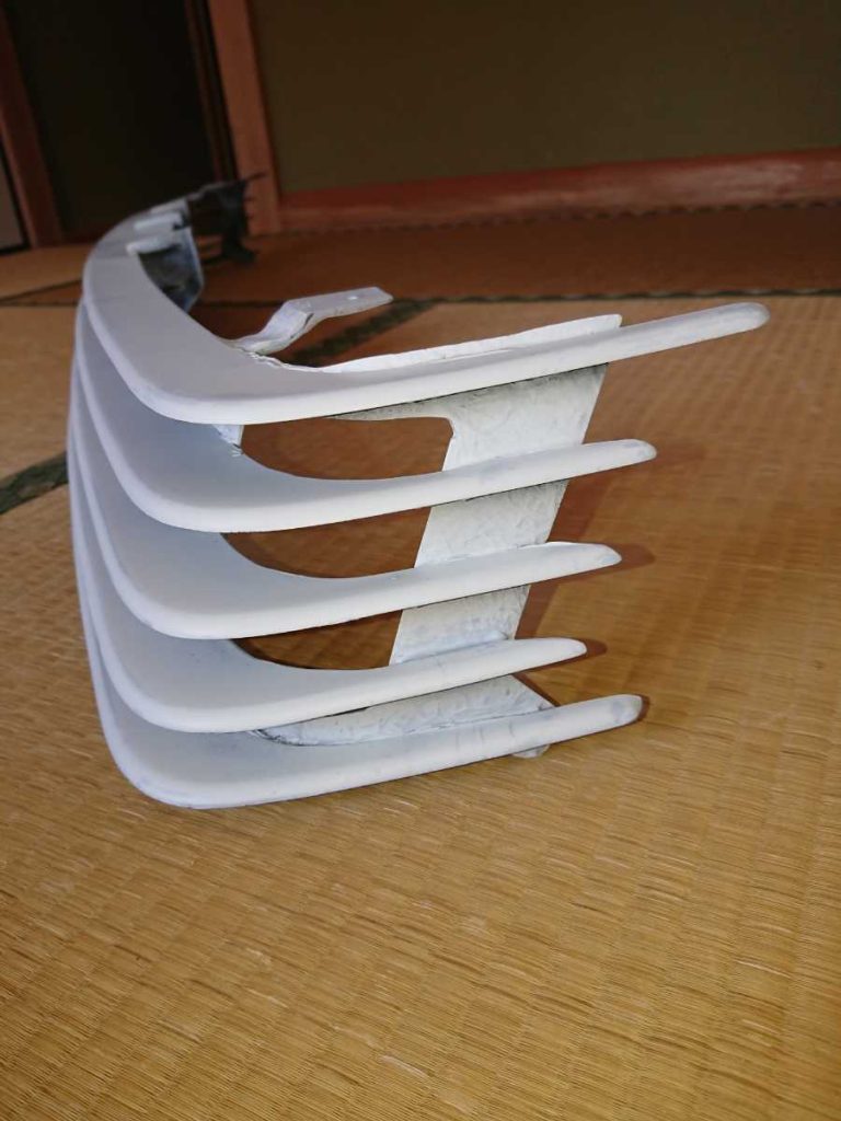 Close-up of a white car bumper grille on a tatami mat, showcasing vertical slats and their detail in a traditional Japanese room.