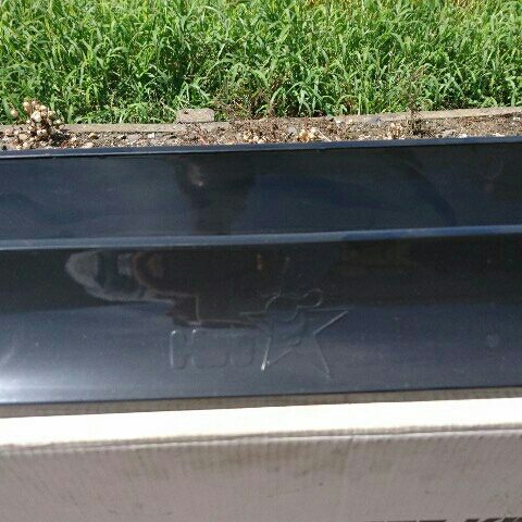 Close-up of shiny black plastic object with logo and Japanese text 'ホムセンター' (Home Center), placed outdoors near grass.