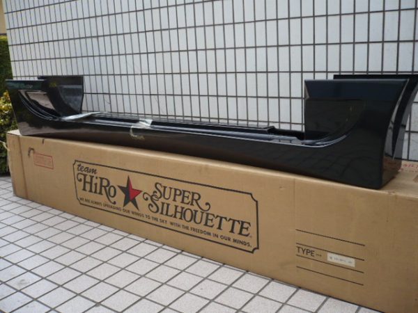 Black Team Hiro Super Silhouette rear wing on a cardboard box against a tiled wall.