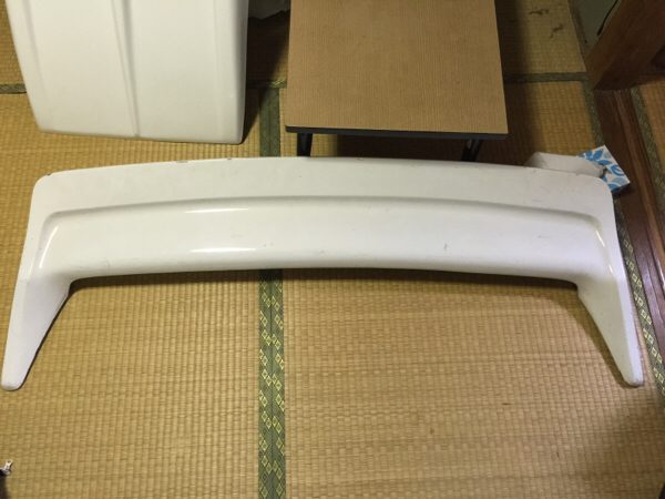 White car spoiler placed on a tatami mat in a traditional Japanese room, with a table and cupboard in the background.