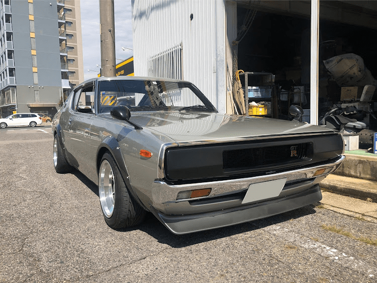 Classic gray Nissan GT-R parked in front of an auto repair shop on a sunny day. Japan street scene.