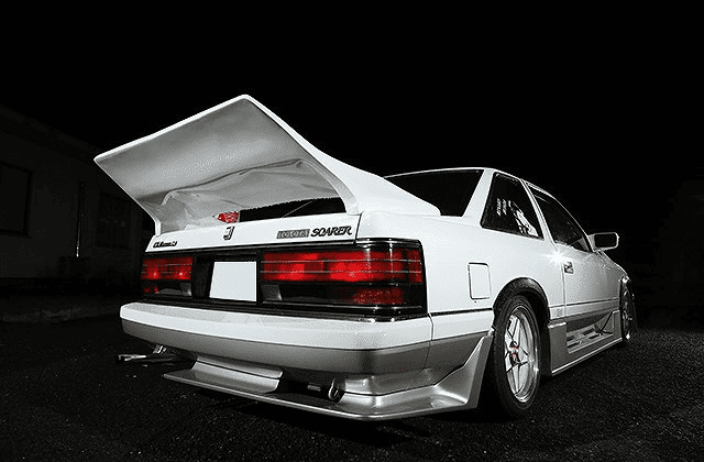 Modified white Toyota Soarer with large rear wing parked at night, showcasing custom body kit and performance enhancements.
