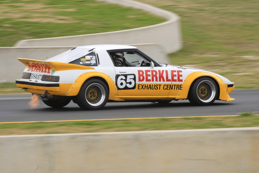 Vintage race car with Berklee Exhaust Centre branding on track, flames visible from exhaust. Car number 65.