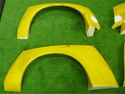 Two yellow car fender flares placed on a green surface, with minor damages visible on the pieces.