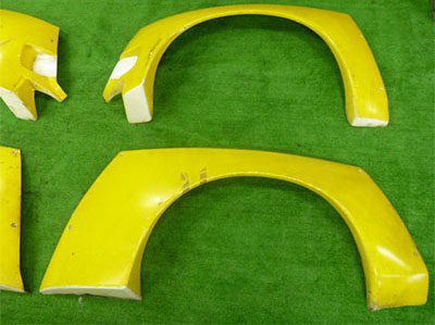 Yellow car fender flares on a green surface with minor wear and tear visible.