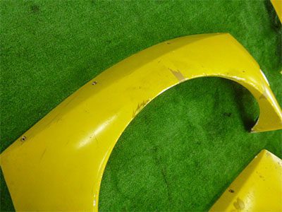 Yellow car fender on green grass background, showing slight wear and tear. Japanese text visible: ボディパーツ (Body parts)