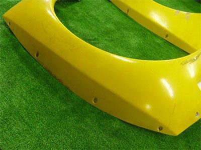 Yellow car bumper on a green grass surface; close-up view showing attachment points.