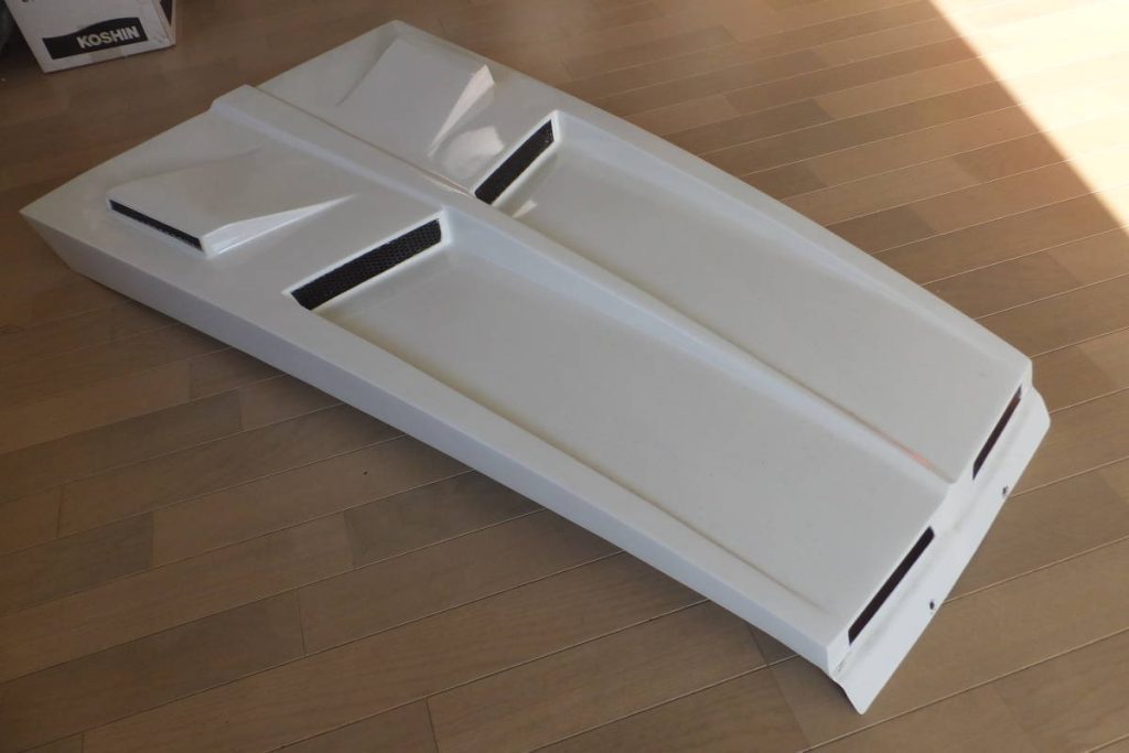 White fiberglass car hood with air vents on wooden floor, Koshin box in the background.