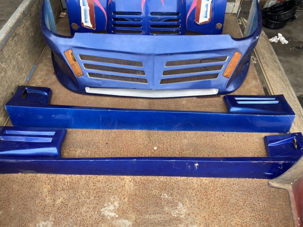 Blue aftermarket car body kit, including front bumper and side skirts, displayed on a rusty metal surface.