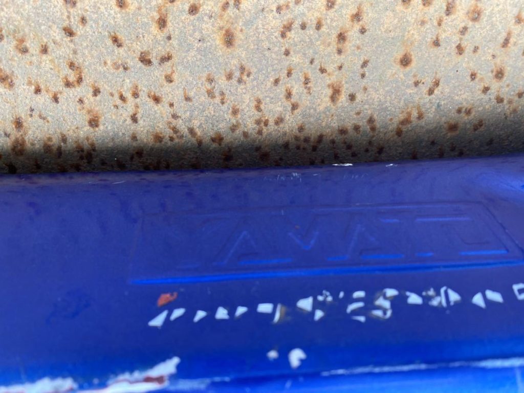 Close-up of a rusty metal surface above a blue plastic object with faint Japanese text, suggesting wear and age.