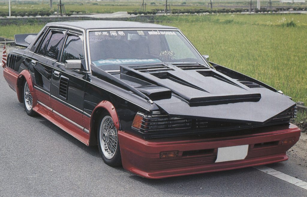 Custom heavily modified Japanese Bosozoku style car with exaggerated body kits, parked on roadside.