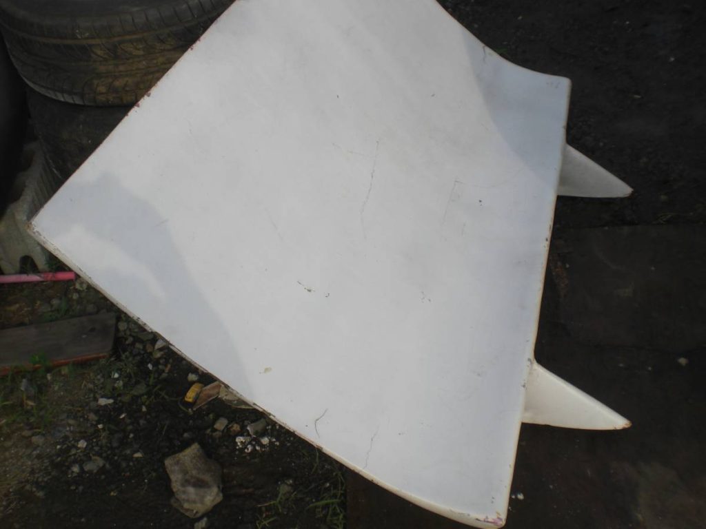 Damaged car hood placed against stacked tires, surrounded by scattered debris on the ground.