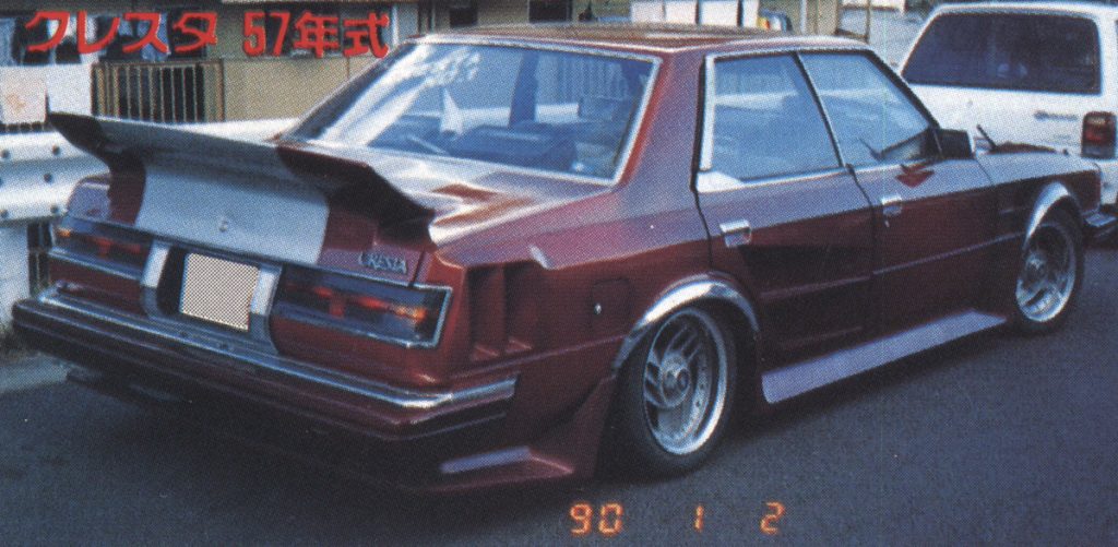 Japanese Cresta 57 Year Model, red modified classic car with wide body kit and spoiler, rear view on street.