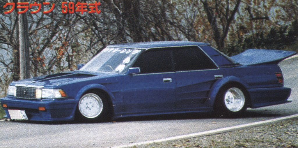 Modified blue Crown car from 1984 on a forest road in Japan. Japanese text: クラウン 59年式 meaning Crown, 1984 model.