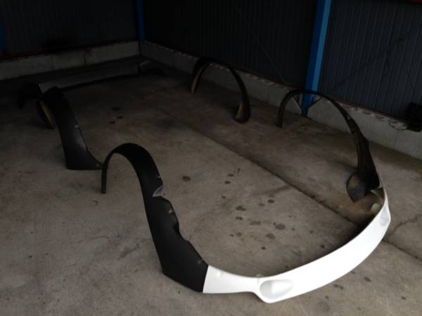 Nissan Fairlady Z S30 Works fender body kit components laid out on garage floor, including fenders, bumper, and side skirts, in preparation for installation.