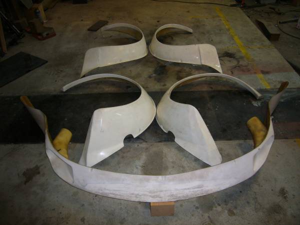 Custom fiberglass Nissan Fairlady Z S30 Works fender body panels for car modification, including fender flares and bumper parts, laid out on workshop floor.