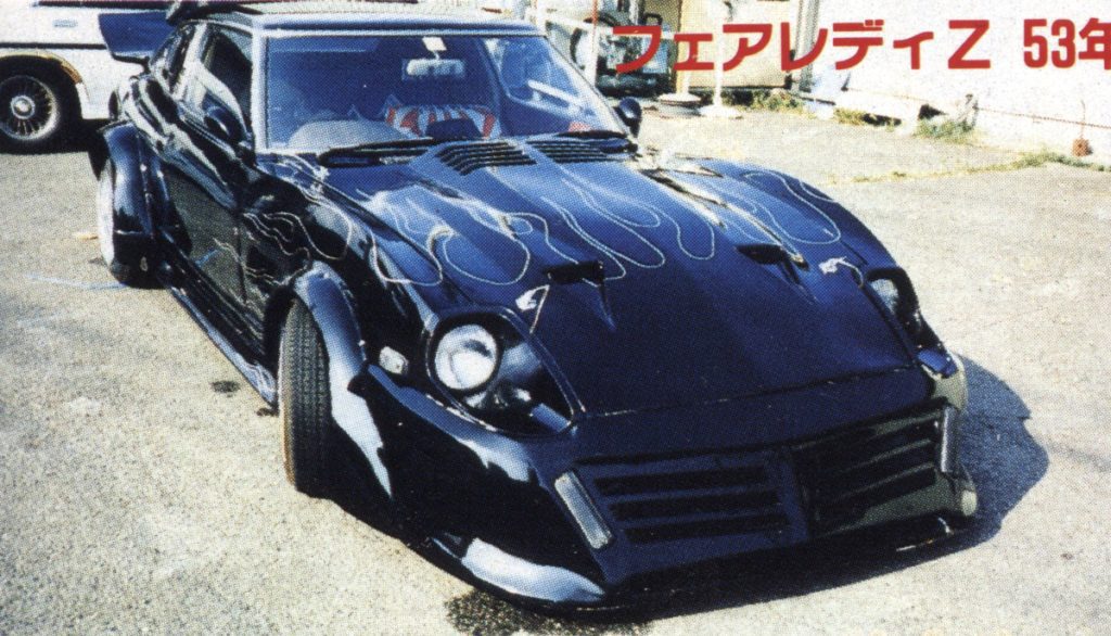 Customized black Nissan Fairlady Z with flame decals, 53 years old (フェアレディZ 53年), classic car in parking lot.