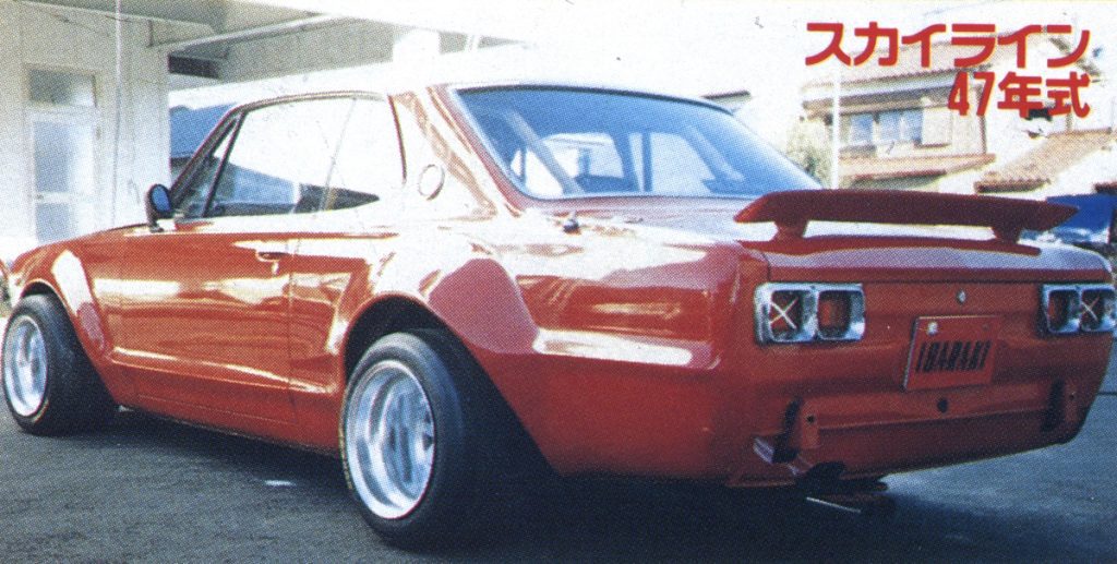 Vintage red Nissan Skyline car from 1972 with wide body kit, rear view at Japanese car meet. Text reads Skyline, 47th model year.