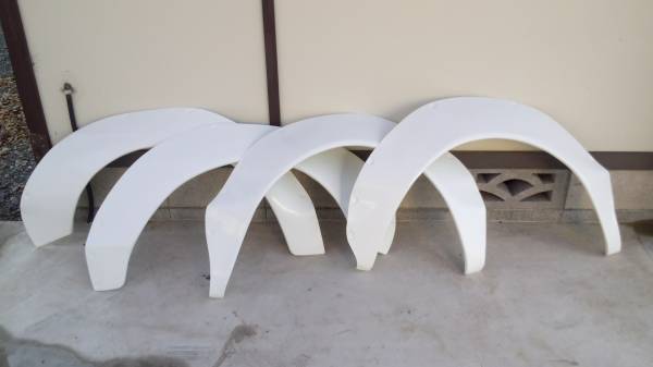 Four white car fender flares aligned on a concrete floor against a beige wall with a Japanese design element.