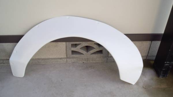 White car fender placed on floor against wall, ready for installation. Perfect for automotive accessories or repair businesses.