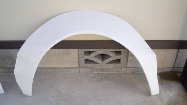 White automotive fender placed against a wall for display. Cinder block behind and concrete floor below.