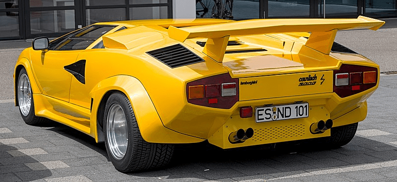 Yellow Lamborghini Countach 5000 S, rear view showing iconic design and spoiler, displayed outdoors on a paved surface.