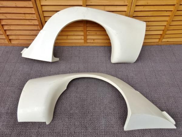 White car fender flares placed on a gray carpet with wooden wall background.