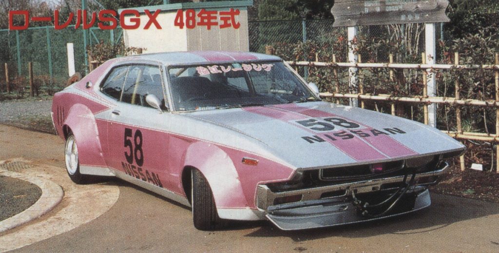Vintage pink and silver Nissan Laurel SGX c130 from 1973 with decals and Savanna Works fenders showing Kanji characters, parked outdoors.
