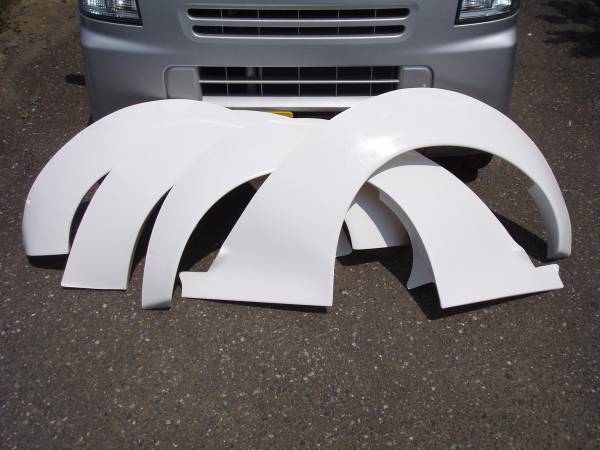 White car fender flares placed in front of a vehicle's grille on a paved surface, highlighting automotive parts for customization.