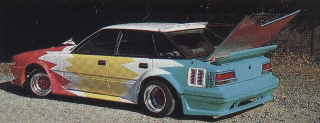 Colorful custom car with geometric paint design and exaggerated rear wing.(Note: No Japanese text is visible in the image.)