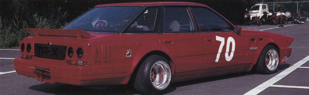 Red racing car number 70 with rear wing spoiler and TR-X license plate, parked in an outdoor parking lot.