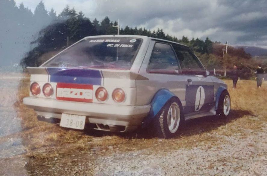 Vintage modified Mazda car with a number 10 decal parked on a field, featuring MAZDA and RACING WORKS stickers.