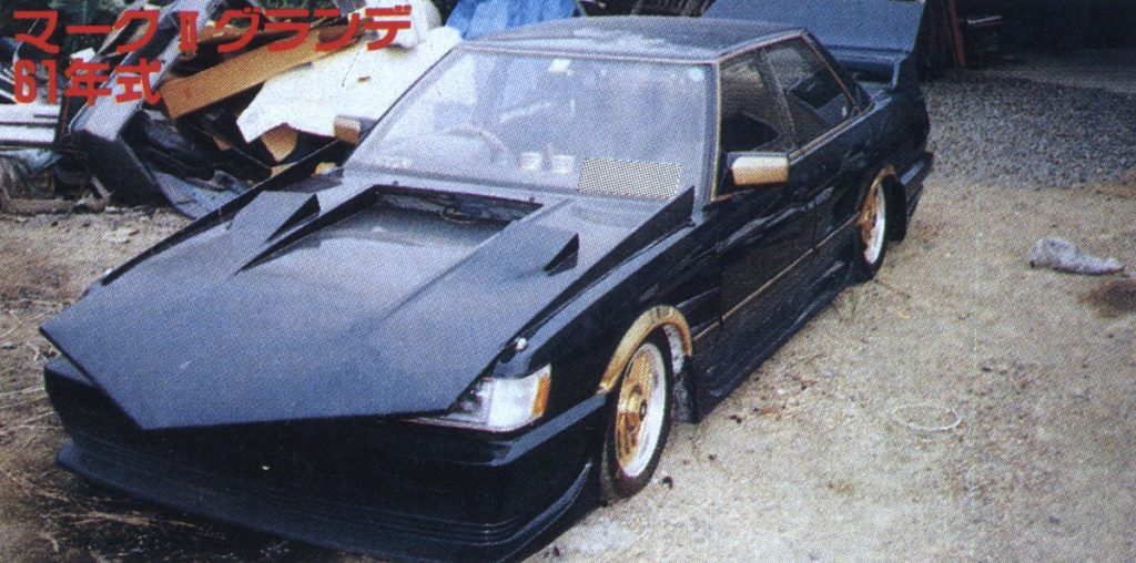 Custom black 1986 Toyota Mark II Grande with modified hood and gold rims, parked in a garage surrounded by items.(Note: マークIIグランデ 61年式 translates to Mark II Grande 1986 model)