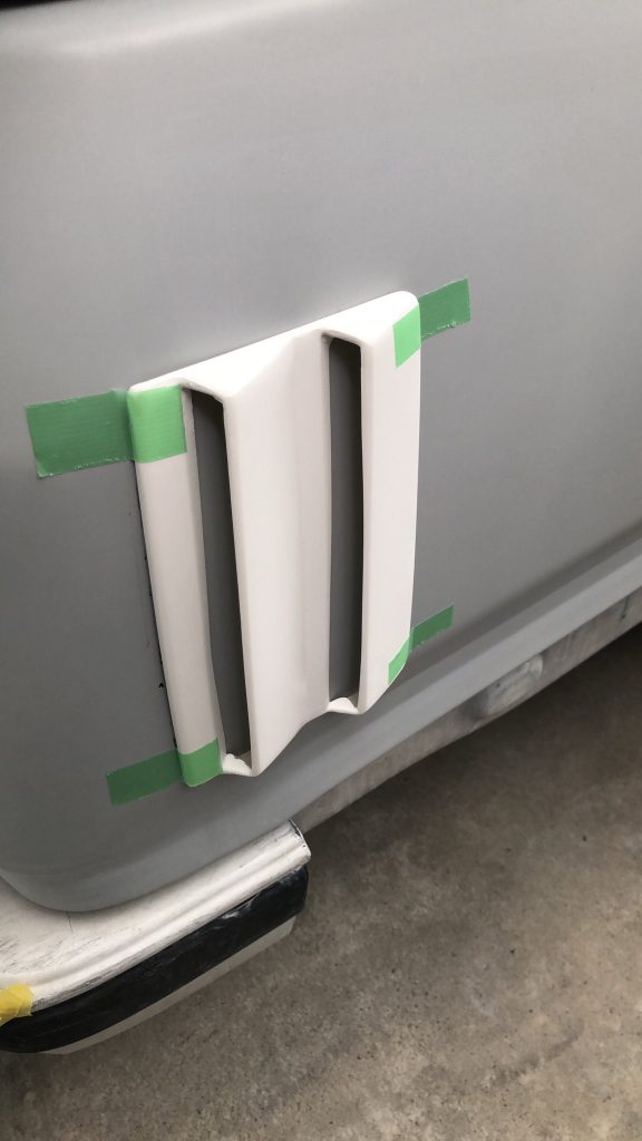Custom car body part prototype taped to vehicle for fitting on a repair shop floor.