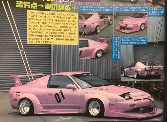 Customized pink drift car with wide-body kit, aftermarket wheels, large rear wing, and number 01 on the door, in a garage setting.
