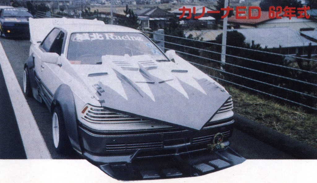 Modified Toyota Carina ED with custom body kit and large hood scoop, styled in Japanese Bosozoku fashion. Text: Carina ED 1987.