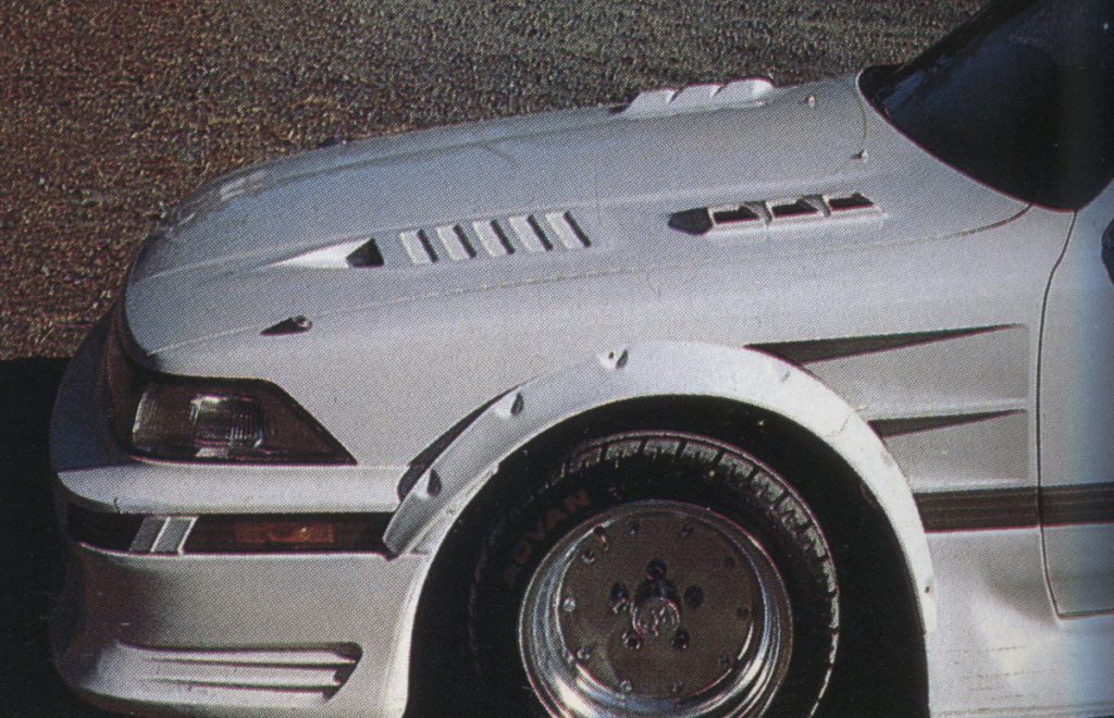 Close-up of a modified white sports car's front left side, featuring stylish vents, detailed headlights, and ADVAN tire text.