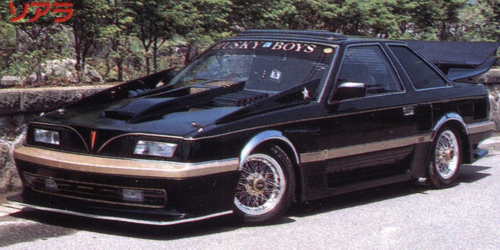 Modified black retro car parked outdoors, featuring Husky Boys on the windshield and ソアラ (Soarer) in Japanese text.