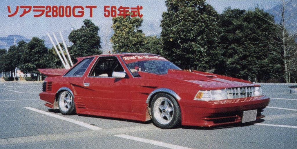 Red Toyota Soarer 2800GT 1981 model in parking lot with Japanese text above car; modified classic JDM car.