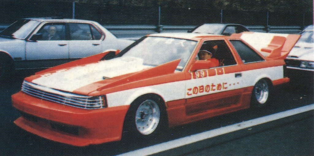 Modified white and red car with Japanese text この日のために meaning For this day on the side, parked on a road.