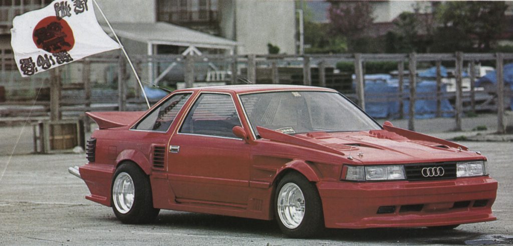 Red custom car with Audi grille and Japanese flag featuring a black bull and text that reads 必勝 (certain victory) and 俺道 (my way).